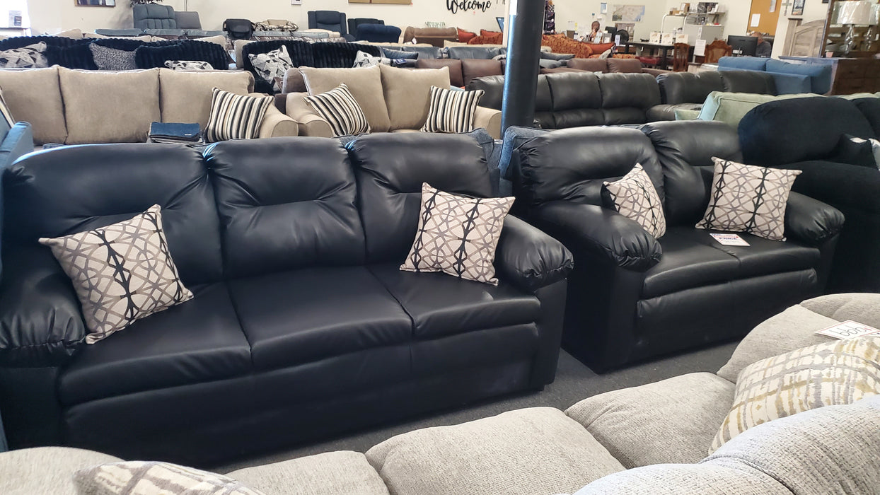 Black leather sofa and loveseat set with patterned toss pillows in a showroom setting
