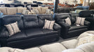 Black leather sofa and loveseat set with patterned toss pillows in a showroom setting